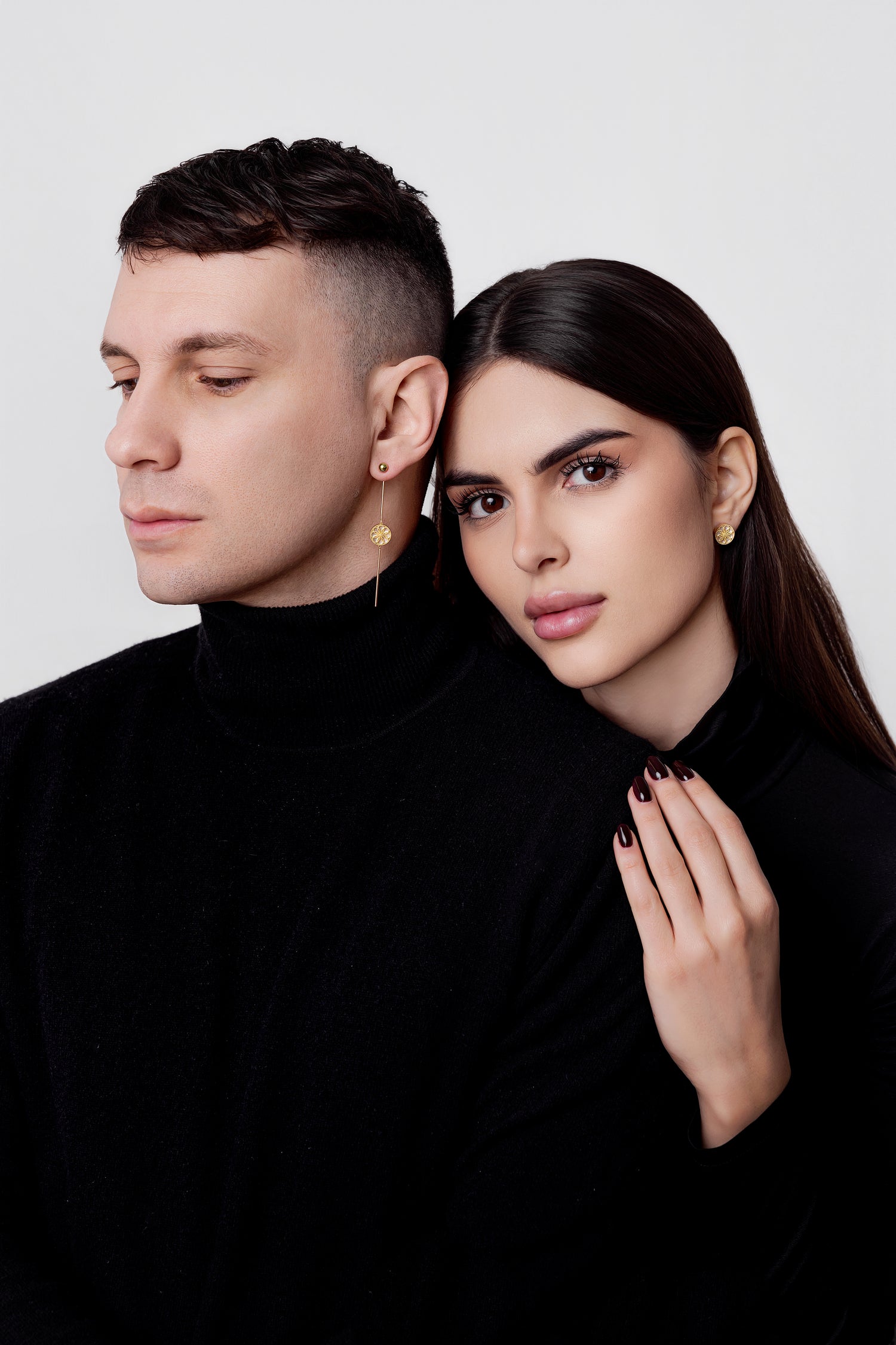 Two people wearing gold earrings against a white background. She is wearing Ravenna White Mother of Pearl Stud Earrings in 18kt Yellow Gold. He is wearing The Ravenna White Mother of Pearl 3-in-1 Long Earrings in 18kt Yellow Gold.