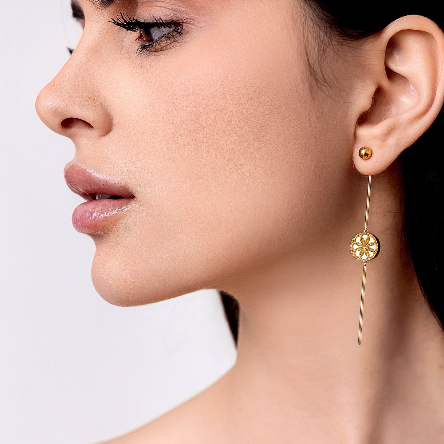 Close-up of a woman wearing gold earrings, The Ravenna White Mother of Pearl 3-in-1 Long Earring in 18kt Yellow Gold. She is wearing the vintage look drop earring.