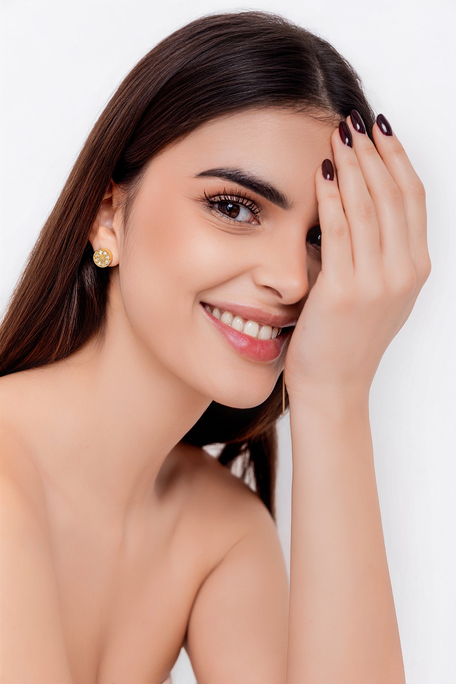 Woman with a bright smile, wearing gold earrings, against a white background. She is wearing the Ravenna white mother of pearl stud earrings in 18kt yellow gold.