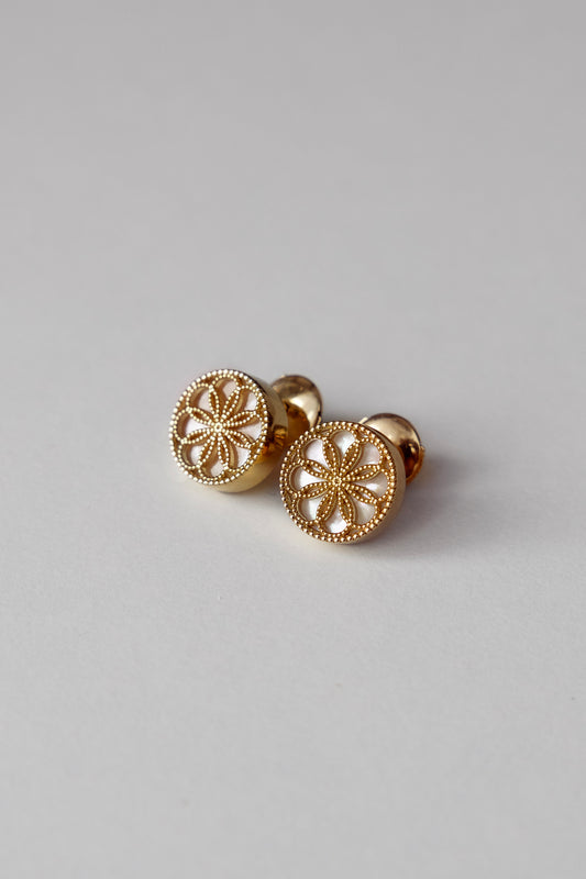 Gold earrings with a byzantine inspired design on a light grey background. The Ravenna White Mother of Pearl Stud Earrings in 18kt Yellow Gold.