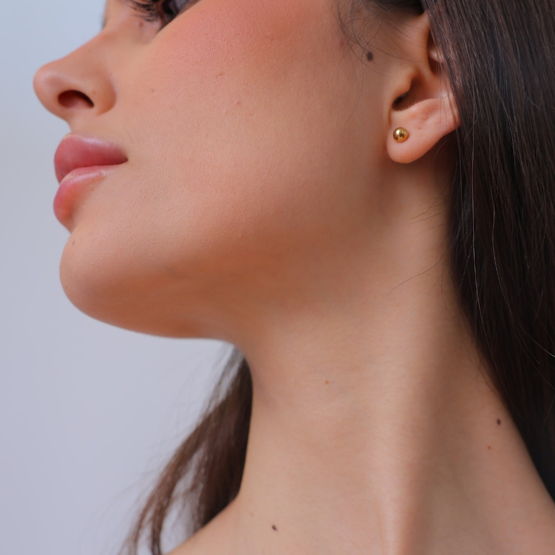 Close-up of a woman's neck and ear with a gold earring, The Ravenna White Mother of Pearl 3-in-1 Long Earring in 18kt Yellow Gold. She is wearing the classic option featuring an 18kt gold bubble stud earring, perfect for everyday wear.