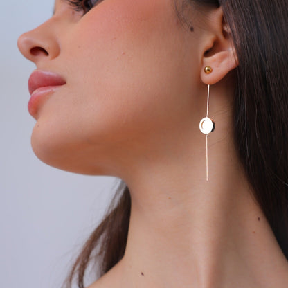 Close-up of a woman wearing a gold earring, The Ravenna White Mother of Pearl 3-in-1 Long Earring in 18kt Yellow Gold. She is wearing the drop earring with a minimalist look featuring plain polish gold and mother of pearl.