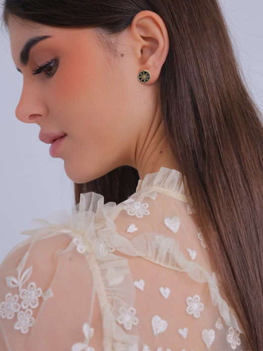 Close-up of a woman wearing earrings with a plain background. A pair of Gold earrings with a byzantine inspired design. The Ravenna Black Onyx Stud Earrings in 18kt Yellow Gold. 