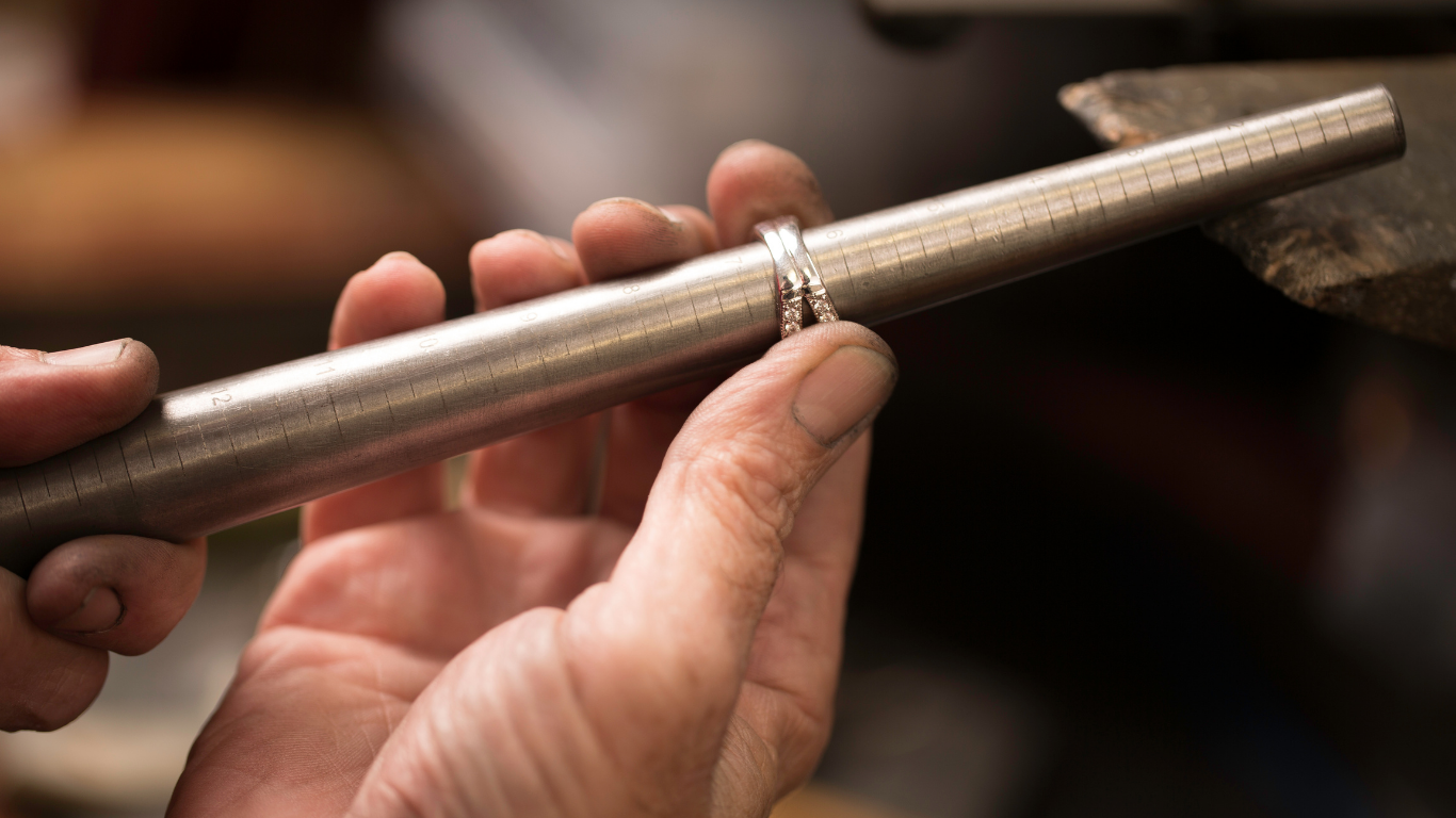 Close-up of hands holding a metal rod to measure ring sizes, with a blurred background