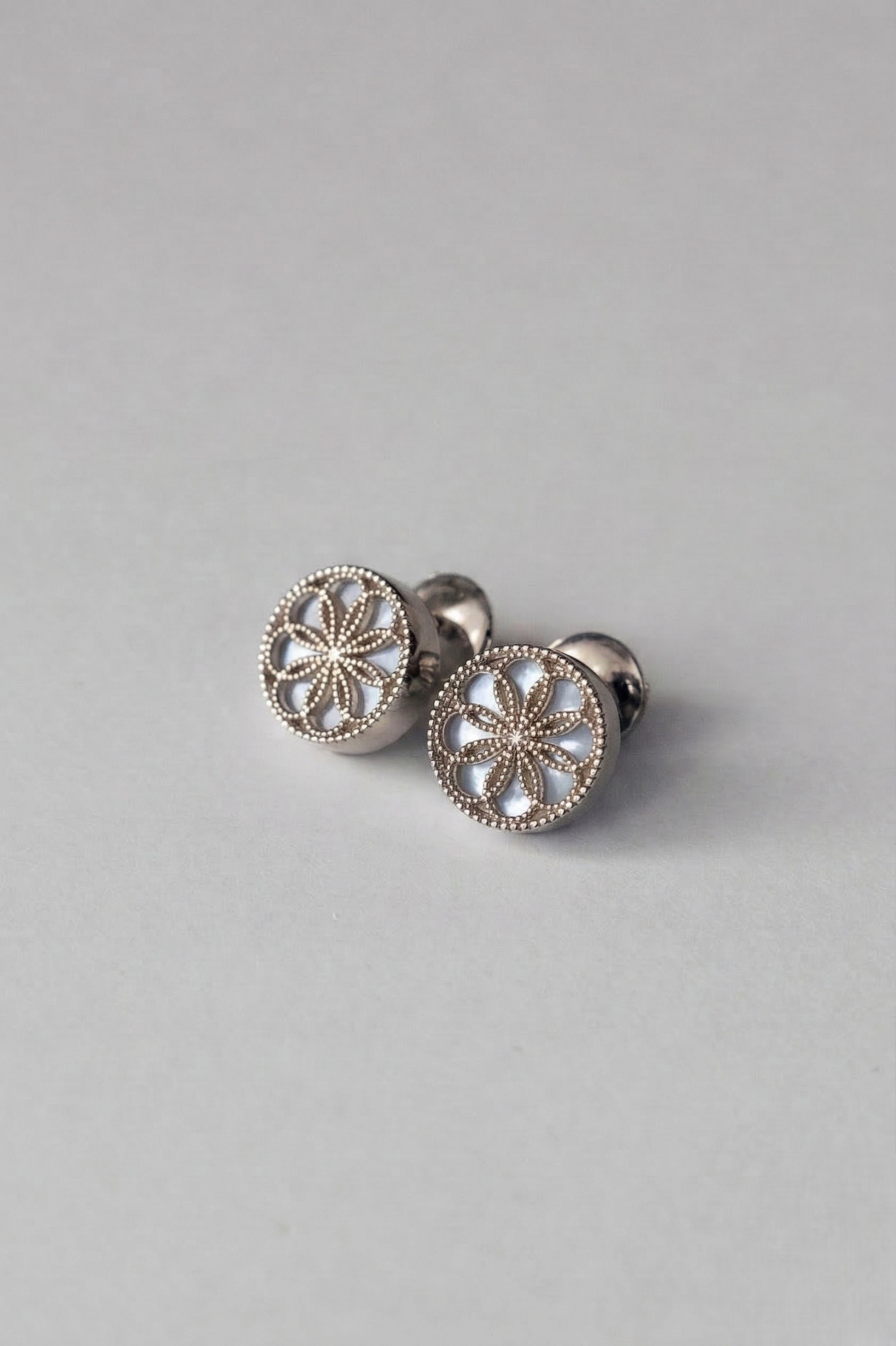 Gold earrings with a byzantine inspired design on a light grey background. The Ravenna White Mother of Pearl Stud Earrings in 18kt White Gold.