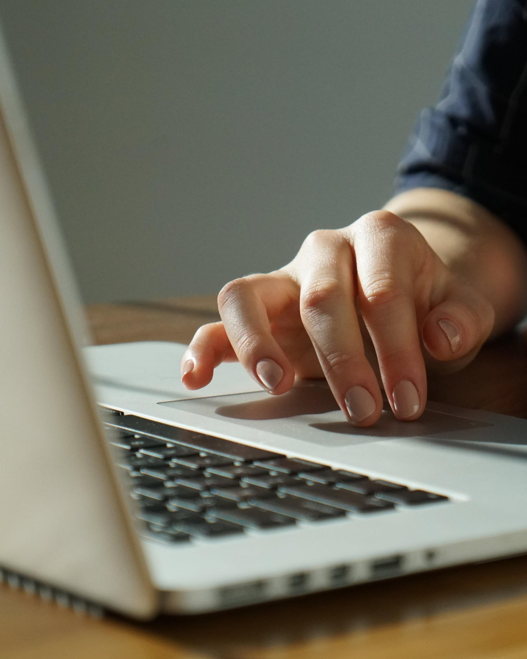 Hand typing on a laptop keyboard with a neutral background. The bespoke process and handling.